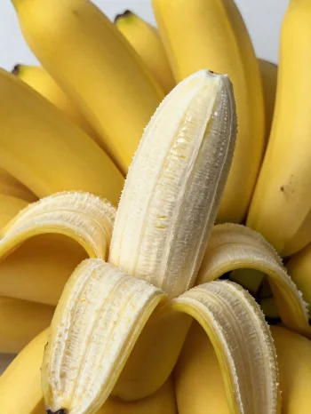 Banană proaspăt feliată și întreagă, în bol și pe masă rustică